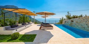 Zona de piscina con mobiliario, sombrillas y vista al mar.