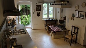 A kitchen with a gas stove, a hanging light fixture, and a window with a view of greenery. - Lake Garda: Idyllic villa in quiet village center with olive and palm trees garden (Nago-torbole)