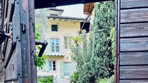 A rustic wooden door leading to a cobblestone courtyard with a building in the background. - Lake Garda: Idyllic villa in quiet village center with olive and palm trees garden (Nago-torbole)