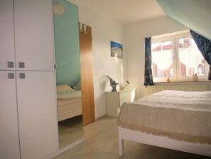 A bedroom with a bed, a dresser, a mirror, and a window with curtains.