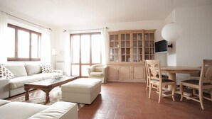 A spacious living room with a sofa, ottoman, and a wooden coffee table. There is a dining area with a wooden table and chairs, and a cabinet with glass doors. - Nido delle Campane - Romantic apartment with 2 terraces with panoramic-sea views (Castiglione della Pescaia)