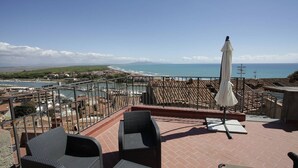 A terrace with wicker chairs and a white umbrella, overlooking a coastal town and the sea. - Nido delle Campane - Romantic apartment with 2 terraces with panoramic-sea views (Castiglione della Pescaia)