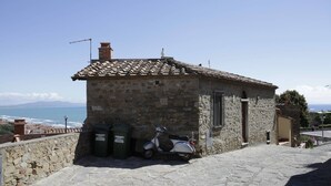 A stone building with a tiled roof, a scooter parked in front, and a view of the sea. - Nido delle Campane - Romantic apartment with 2 terraces with panoramic-sea views (Castiglione della Pescaia)