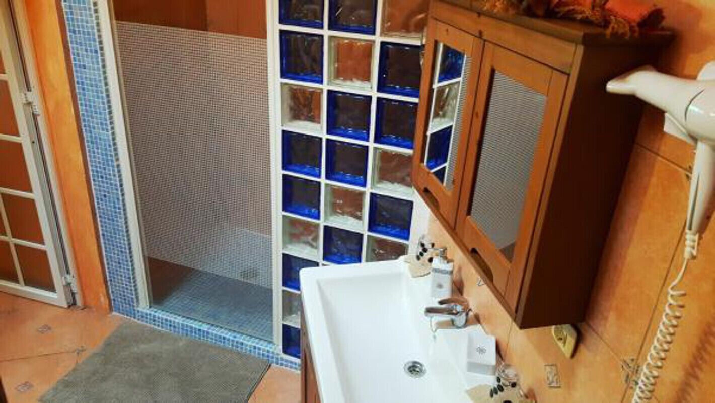 Une salle de bain avec un lavabo blanc, un meuble en bois et un espace douche aux carreaux de verre bleus.