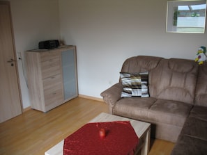 Ein Wohnzimmer mit einem braunen Sofa, einem Holzschrank und einem roten Tisch.