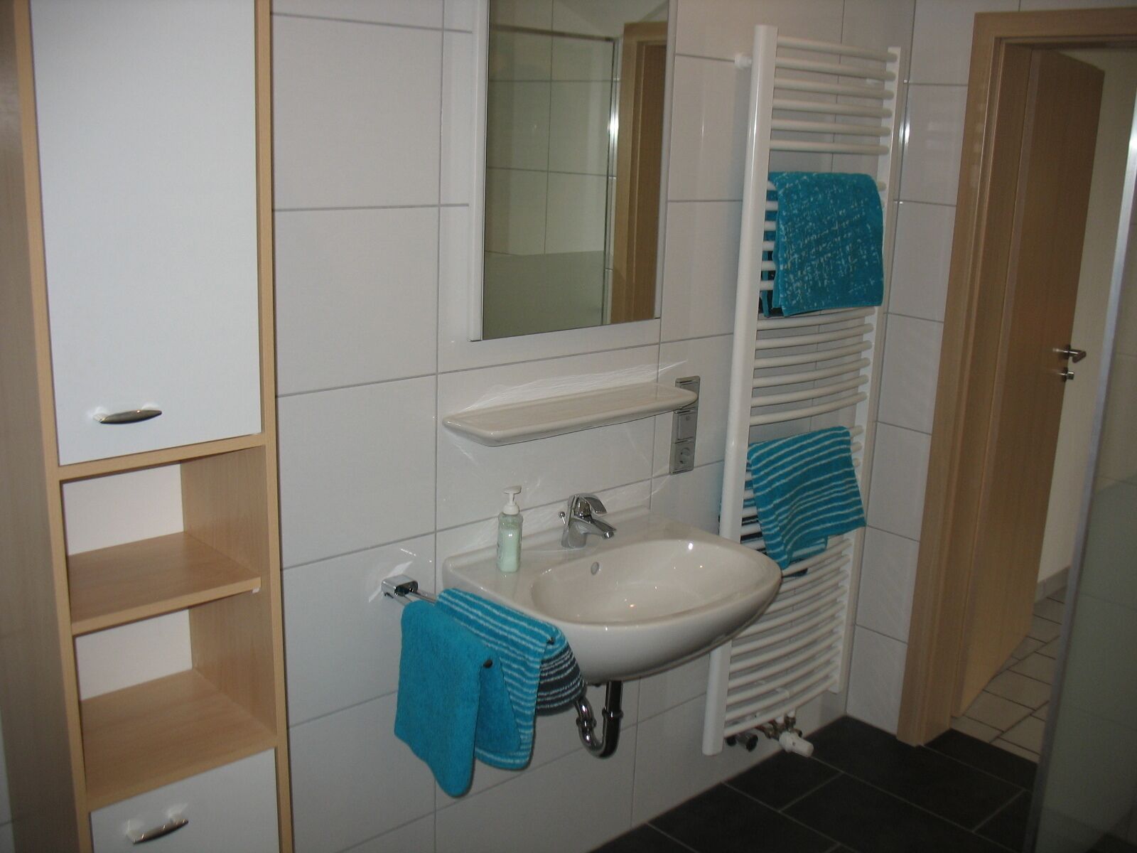 A bathroom with a white sink, a mirror, a towel rack, and a wooden cabinet.