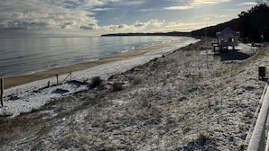 Une plage avec une petite maison sur pilotis, un ciel dégagé et le soleil se couchant ou se levant.