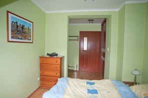 Een slaapkamer met een houten dressoir, een bed met een beddeken met patroon, een deur en een ingelijste foto aan de muur.