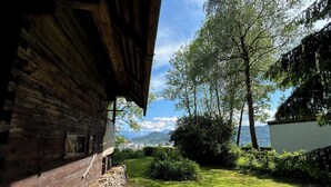 Un edificio de madera rústico con pared de piedra, patio cubierto de césped y vistas a montañas y un lago.