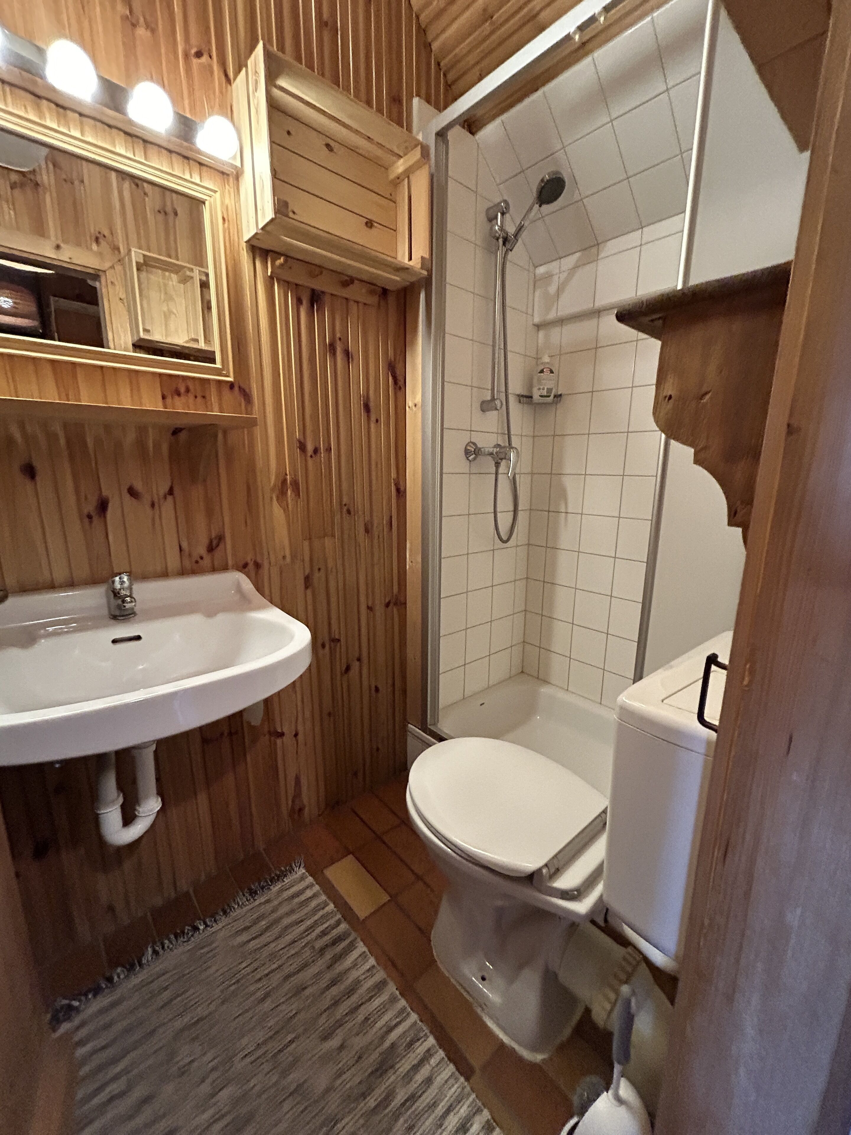 Un baño con paneles de madera, un lavamanos blanco, un inodoro y una ducha.