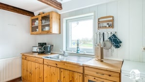 Una cocina con armarios de madera, horno empotrado, ventana con vistas y diversos utensilios de cocina colgados en la pared.