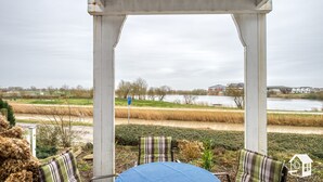 Un área de estar techada al aire libre con vista a un lago y edificios residenciales.