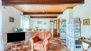 Una sala de estar acogedora con techo de madera, televisor sobre un mueble bajo, sillón estampado y suelo de baldosas.