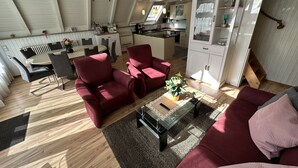 A spacious living area with a dining table, red chairs, a glass coffee table, and a red sofa. A kitchen is visible in the background with white cabinets and a wooden countertop. - With sauna and fireplace (Rheinboellen)