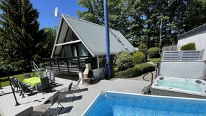 A pool area with a hot tub, outdoor seating, and a barbecue grill. - With sauna and fireplace (Rheinboellen)