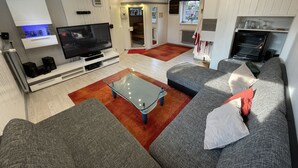 A modern living room with a flat-screen TV, a glass coffee table, a grey sofa, and a built-in oven. - With sauna and fireplace (Rheinboellen)