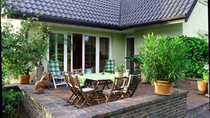 Eine Terrasse mit Tisch und Stühlen, umgeben von Kübelpflanzen und einer Backsteinmauer.