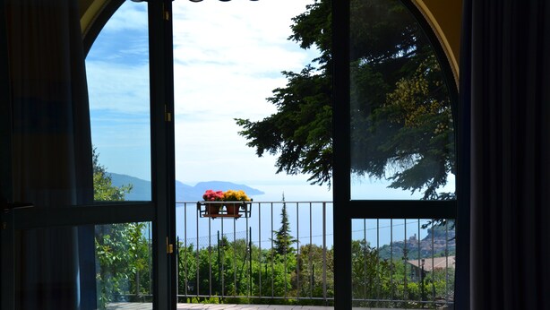 Une vue depuis un balcon orné d’une rambarde en métal, d’un pot de fleurs et d’un paillasson.