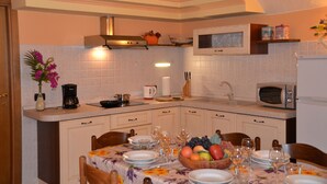 Une cuisine avec des meubles blancs, un four à micro-ondes, un grille-pain et une table à manger dressée avec des assiettes, des verres et un panier de fruits.
