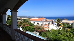 A coastal villa with a view of the sea, surrounded by lush greenery and a white-washed exterior.