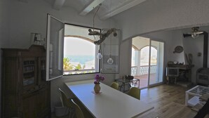 A spacious living area with a large window overlooking a scenic view, a dining table with chairs, and a fireplace.