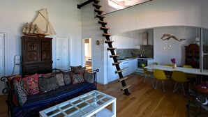 A modern living space with a staircase leading to an upper level, a dining area with yellow chairs, and a ship model on a cabinet.