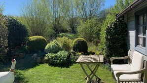 A garden with a wooden table and chairs, surrounded by various plants and a white bird. - Only 250m to the beach - for 4 pers., 70sqm, large balcony. South-facing garden/terrace, conservatory (Schönberger Strand)