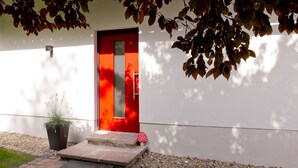 Un bâtiment moderne avec une porte rouge, un pot de fleurs et une décoration en forme de champignon à l’entrée.