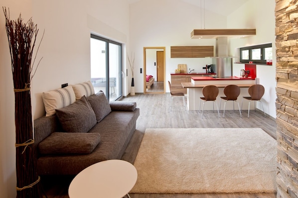 Ein modernes Wohnzimmer mit einer Couch, einem kleinen runden Tisch und einer Küchenzeile mit Esstisch und Stühlen.