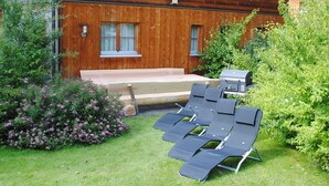 Une maison en bois dotée d’un patio comprenant des chaises longues et un barbecue.