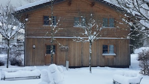 Une cabane en bois avec un toit en pente, entourée d’un paysage enneigé et d’arbres.