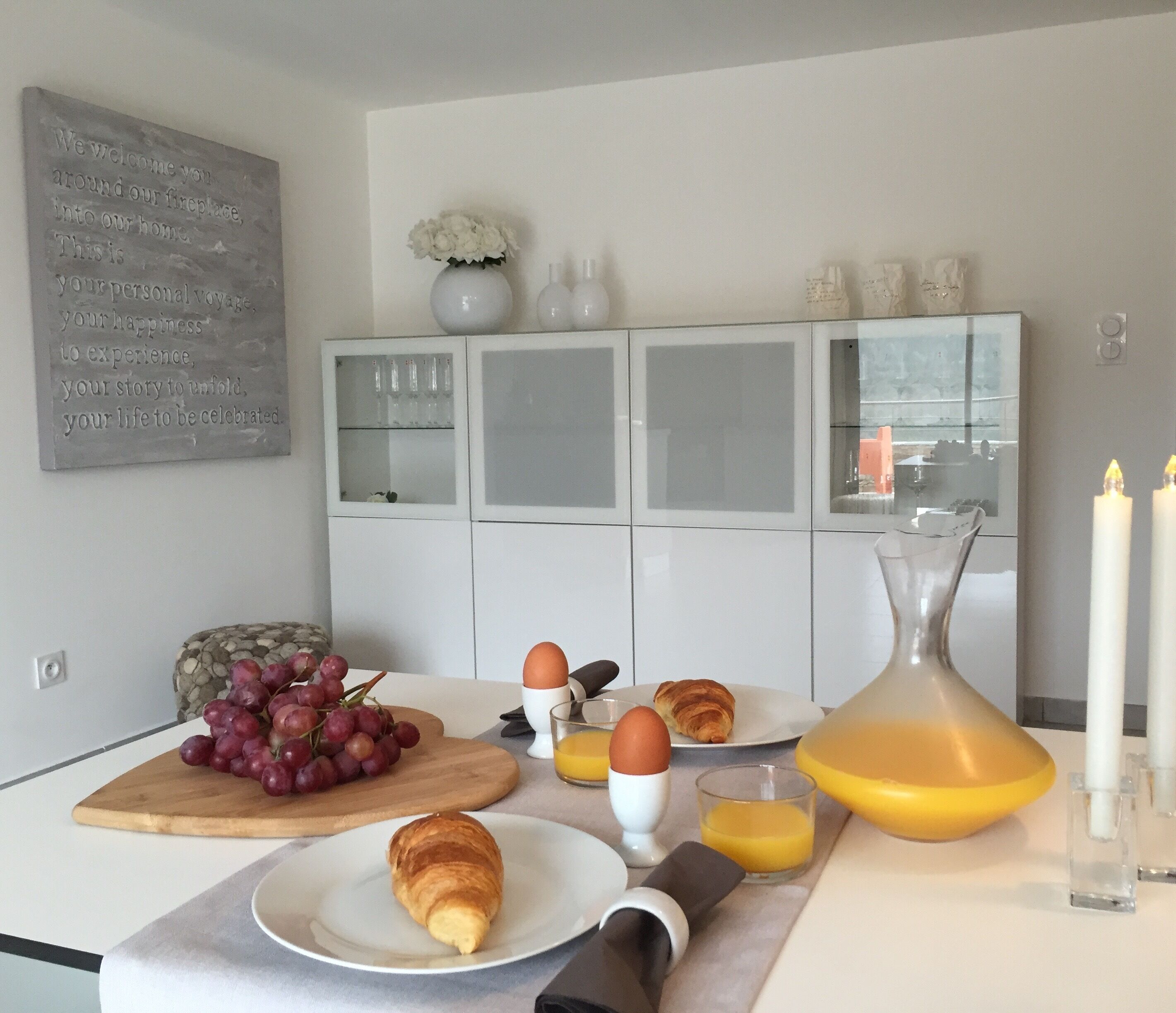A breakfast setup with croissants, grapes, eggs, and orange juice on a modern kitchen counter.