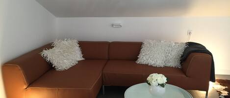 A modern living room with a brown sectional sofa, two white fluffy pillows, a glass coffee table with a white vase, and a cowhide rug.