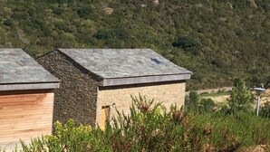Edifici amb façana de pedra i teulada inclinada, envoltat de vegetació i turons.