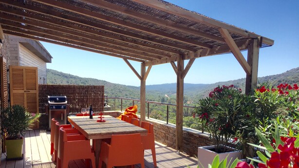 Terrassa a l'aire lliure amb taula i cadires de fusta, una barbacoa i plantes en testos.