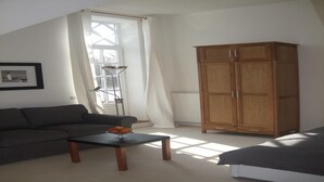 Una sala de estar con un sofá, una mesita de centro con fruta, un armario de madera y una ventana con cortinas.