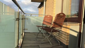 Una terraza de madera con dos sillas de madera y una barandilla de vidrio.