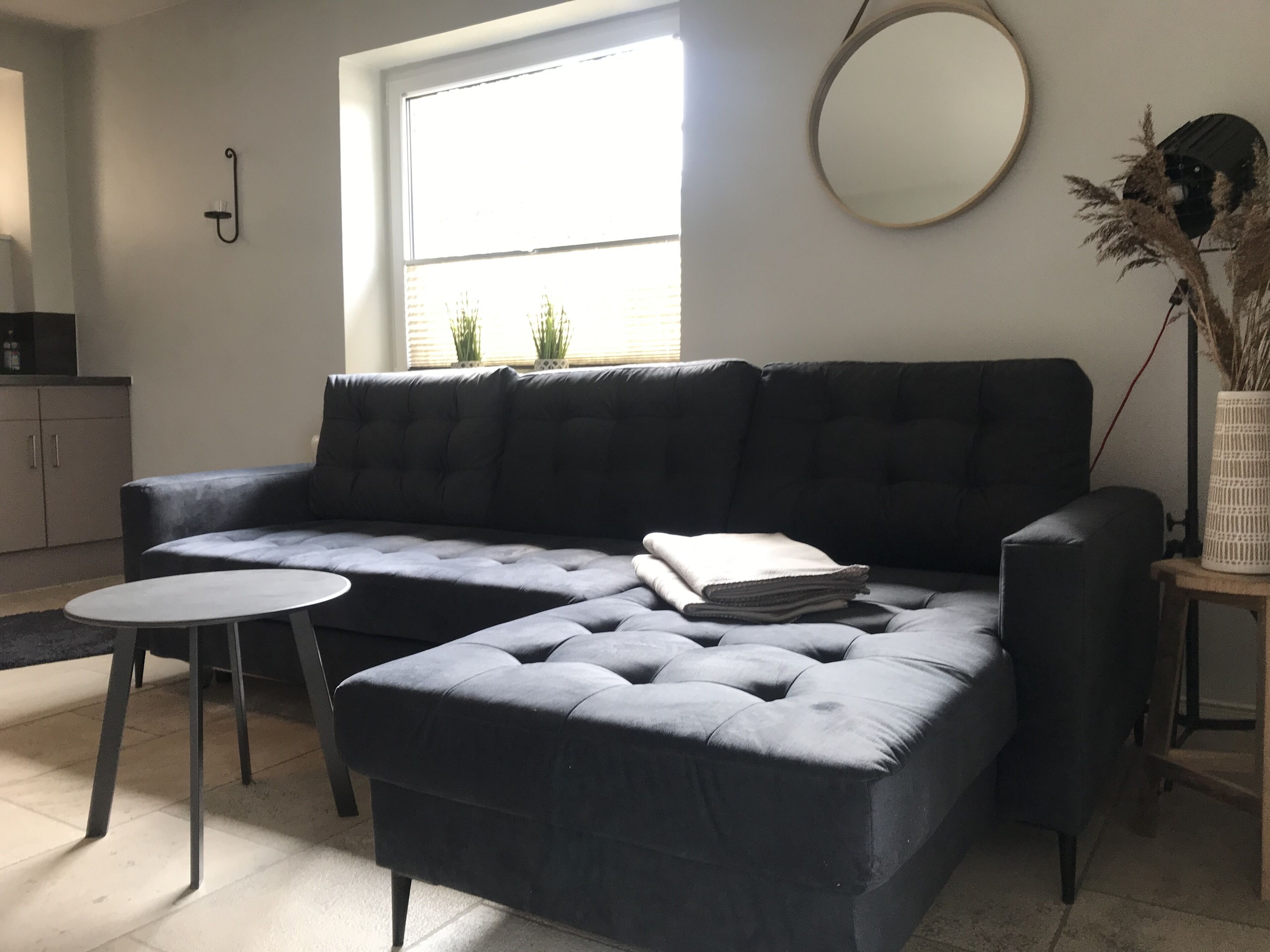 Una sala de estar moderna con un sofá seccional azul oscuro, una mesita redonda y un espejo circular en la pared.