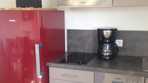 Una cocina compacta con un refrigerador rojo, un microondas, una cafetera y un lavavajillas.