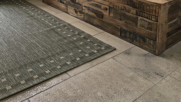 Un dormitorio con cabecera de madera, cama con ropa de cama gris, un radiador, una ventana con persianas y una planta.