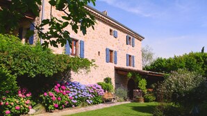 A stone building with blue shutters, a well-maintained lawn, and a variety of flowering plants.