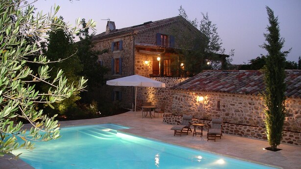 A stone building with a swimming pool, outdoor seating, and a well-lit patio area.