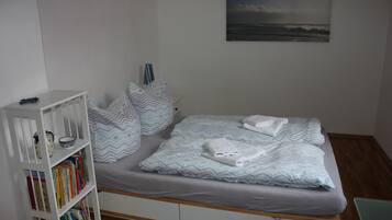 Ein Schlafzimmer mit Bett, Kissen, einem Bücherregal und einem Bild an der Wand.