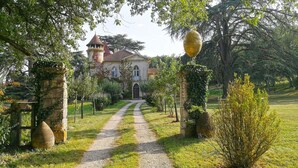 Un edificio histórico con una torre central, rodeado de un jardín bien cuidado y un sendero de grava que lleva a la entrada.