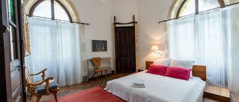 A bedroom with a bed, a chair, a wooden headboard, a red rug, and a wooden door.