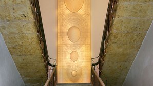Una imponente escalera con barandilla de madera, escalones de piedra y un revestimiento decorativo con diseños circulares.