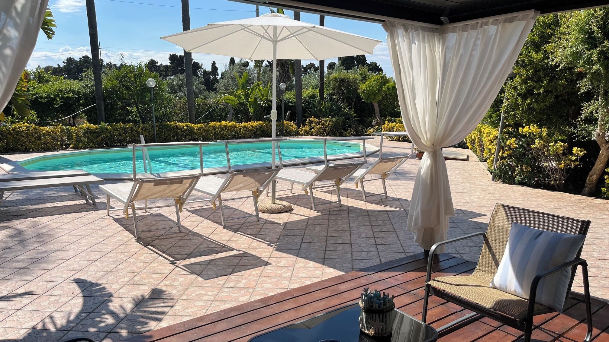 Ett område vid poolen med solstolar, en pool och en möblerad sittplats under tak.