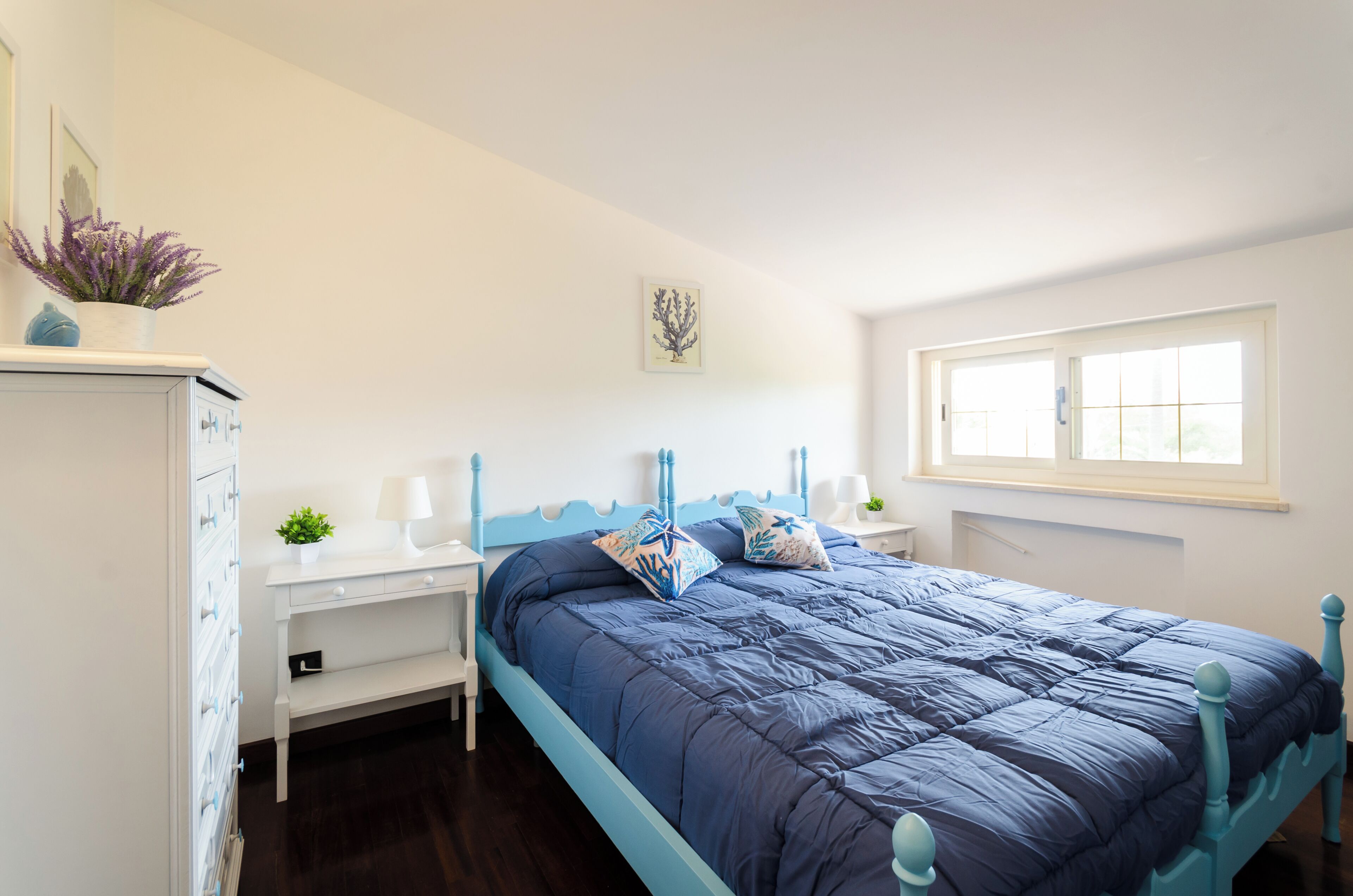 Une chambre à coucher avec un lit, un bureau, une chaise, une fenêtre et une plante.