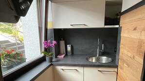 A compact kitchen with a black countertop, white cabinets, a stainless steel sink, and a window with a view of greenery. - Detached vacation home with sauna and whirlpool for individual use (Thüringen)
