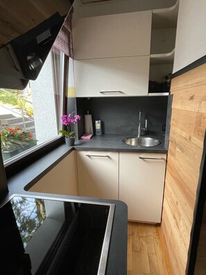 Eine kleine Küche mit schwarzer Arbeitsplatte, weißen Schränken, einer Edelstahlspüle und einem Fenster mit Blick auf Grünflächen.